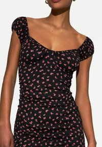 Haut floral noir avec des manches courtes et bouffantes. Présente un design ajusté avec de petits motifs floraux roses et verts. Tissu doux et texturé.