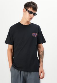 Zwarte katoenen T-shirt met een grafische logo in oranje en blauw op de linkerkant van de borst. Losse pasvorm met korte mouwen en een ronde halslijn.