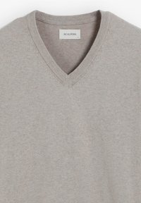 Hellgrauer V-Ausschnitt-Pullover aus weichem Stoff. Verfügt über einen gerippten Halsausschnitt und ein gesticktes Logo auf der Brust. Einfache, glatte Textur.