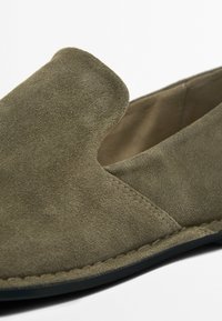Olijfgroene suède instapper met een licht afgeronde neus, blootgestelde stiksels en een zachte textuur. Vlakke zool met een minimalistisch ontwerp.