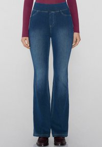 Jeans de mezclilla acampanados con una cintura alta. Color azul medio, ligero desgastado y costuras visibles. Cuenta con dos bolsillos frontales.
