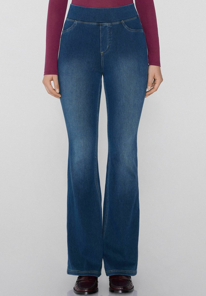 Jeans de mezclilla acampanados con una cintura alta. Color azul medio, ligero desgastado y costuras visibles. Cuenta con dos bolsillos frontales.
