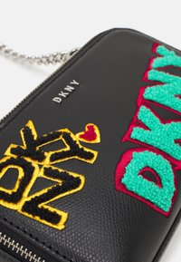 Borsa a tracolla DKNY in pelle nera con lettering ricamato colorato in giallo, rosso e turchese. Ottone argentato e chiusura con zip.