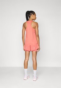 Top deportivo coral con diseño de espalda cruzada, combinado con pantalones cortos a juego que presentan detalles en blanco. Modelo mostrado de espaldas.