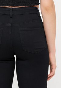 Čierne vysoké jeansy so štíhlym strihom, ktoré majú dve zadné vrecká, hladkú textúru a jemné stehrové detaily.