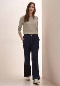Maglione a costine grigio chiaro, pantaloni wide-leg in denim blu scuro e sneakers bianche. L'outfit presenta tasche, cuciture a contrasto e una chiusura con bottoni.