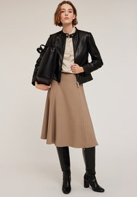 Giacca di pelle nera con chiusura a zip, blusa beige, gonna A-line marrone e stivali neri con tacco alti fino al ginocchio. Include una borsa a tracolla nera.