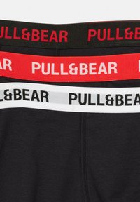 Fekete boxer alsónadrág színes gumis derékrésszel; piros, fekete és fehér "PULL&BEAR" logóval. Sima textúra, szoros illeszkedés.