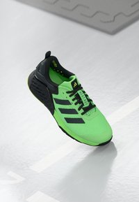 Chaussure de sport Adidas en vert fluo et noir, dotée d'une tige en maille respirante, de trois rayures noires et d'une semelle texturée pour une meilleure adhérence.