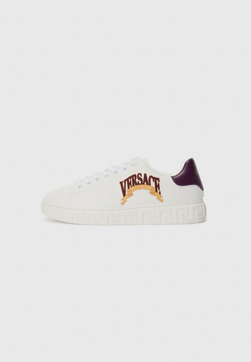 Adidași albi Versace cu un călcâi violet, având un logo auriu și un model decorativ cu chei grecești pe talpă. Material neted, vârf rotund.
