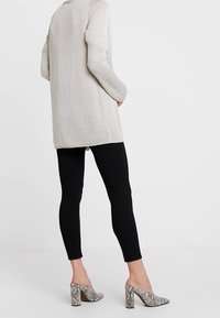 Maglione grigio chiaro a maniche lunghe con una texture a coste abbinato a leggings neri attillati e tacchi grigi con stampa serpente e design a blocco.