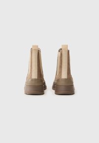 Braune Wildleder-Stiefeletten mit beigen elastischen Seitenpaneelen und einer strukturierten Gummisohle. Der Absatz ist blockartig und verstärkt und verfügt über ein Logodesign.