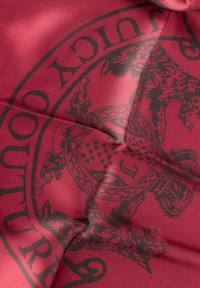 Eșarfă din mătase crimsom, cu un design de logo negru ce prezintă modele și texturi complicate, evidențiind un finisaj luxos și un material neted.