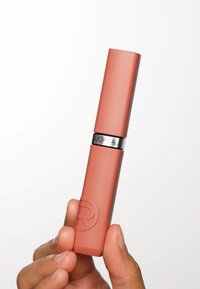 L'Oréal läppstift i matt persiko färg, rektangulär form med ett silverband som har logotypen. Slät textur, hålls i en hand.