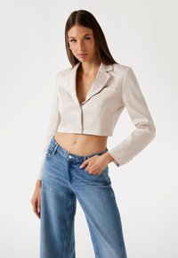 Kroppad gräddfärgad blazer med slagkrage, en ficka och knappstängning, kombinerad med lösa blå denimjeans. Slät textur.