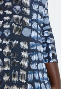 Marinebl�åt stof med abstrakte mønstre af lyse og mørkeblå former, herunder prikker og striber, i et tekstureret design.