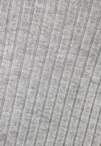 Tissu tricoté gris clair avec une texture côtelée verticale. Présente des rayures alternées plus épaisses et plus fines sur la surface.