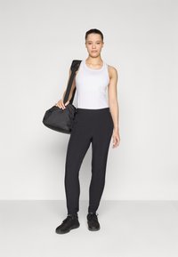 Vit atletisk linne, svarta åtsittande byxor och svarta sneakers. Modellen håller en liten svart väska med axelrem. Enkelt design, inga mönster.