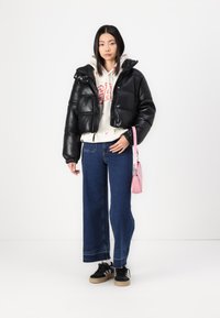 Zwarte gewatteerde leren jas, witte hoodie met rood logo, wijde blauwe jeans, zwarte sneakers met witte strepen en een kleine roze handtas.