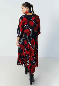 Zwarte jurk met rode bloemenpatronen, witte stelen en een gelaagde uitstraling. Lange mouwen met elastische manchetten, gecombineerd met zwarte hoge laarzen.
