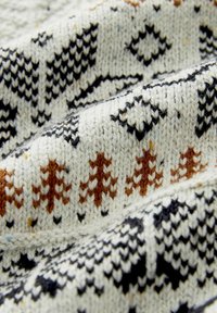 Strickstoff mit einem beigen Hintergrund und schwarzen sowie orangen geometrischen Mustern. Eine Nahaufnahme zeigt die Textur und die geschichteten Falten.