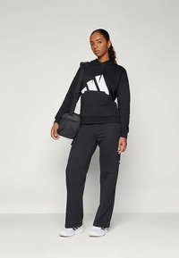 Melnā kapučjaka ar lielu balto grafiku, saskaņota ar melniem sporta biksēm. Modelis nes mazu melnu krustenisko somu. Baltas sporta apavi.