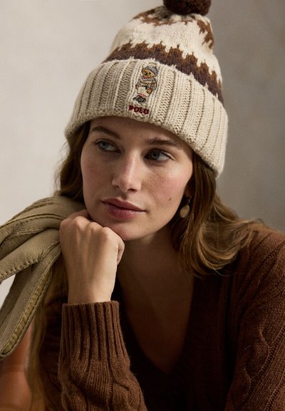 Strikket ulllue i kremfarge med brune geometriske mønstre, toppet med en dusk og med en brodert figur samt "POLO"-merke.