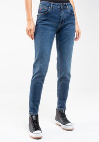 Slim-fit siniset farkut, joissa on hienovarainen haalistuminen, viisi taskua ja vyölenkit. Yhdistetty korkeisiin mustiin tennareihin, joissa on valkoiset pohjat.