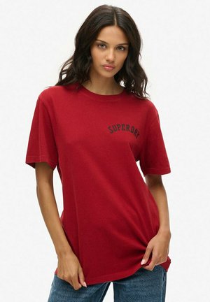 T-shirt en coton rouge à manches courtes, avec un logo noir "SUPERDRY" courbé sur la poitrine. Encolure ronde classique et coupe décontractée.