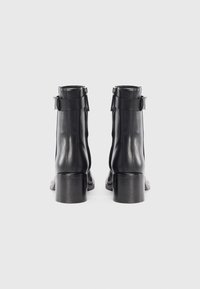 Stivali neri in pelle con tacco quadrato, dettaglio con zip e una fascia attorno alla caviglia. Texture liscia e design elegante.