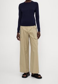 Maglione a maniche lunghe di colore navy abbinato a pantaloni beige a gamba larga e sandali neri. L'outfit presenta design semplici e una vestibilità rilassata.