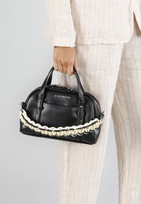 Zwarte leren handtas met een gevlochten crème accent aan de voorkant, voorzien van dubbele handvatten en een ritsluiting, gepresenteerd in een hand-held positie.