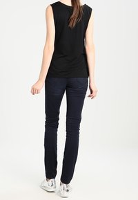 Svart ärmlös topp, marinblå tajta jeans och silverfärgade sneakers. Visad bakifrån, som visar silhuetten och passformen av kläderna.