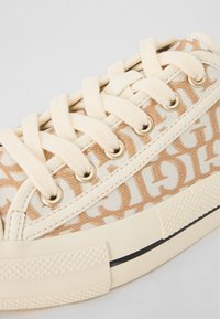 Beiga canvassneakers med ett monogrammönster, gräddfärgade snören, guldfärgade öglor, förstärkt tåhätta och texturerad gummisula.