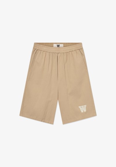 Shorts beiges en tissu léger avec une taille élastique, des poches latérales et un accent logo blanc sur la jambe inférieure gauche.
