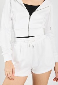 Haut à capuche blanc court avec fermeture éclair et deux poches avant, associé à un short blanc avec cordon de serrage, taille élastique et ourlet cintré.