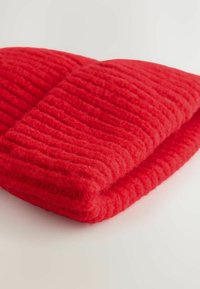 Couverture en tricot rouge pliée avec un motif texturé, reposant sur une surface claire, transmettant chaleur et confort.