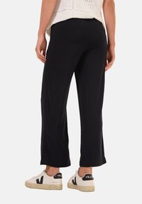 Pantalons larges noirs en tissu extensible, présentant un design décontracté. Associés à des baskets blanches, mettant en valeur une esthétique minimaliste.