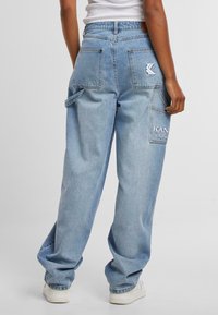 Světle modré denimové cargo kalhoty se širokými nohavicemi, vybavené dvěma zadními kapsami, boční kapsou a vyšívaným logem na pravé kapse.