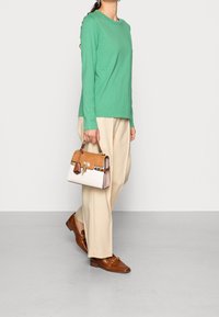Camicia verde a maniche lunghe, pantaloni larghi beige, mocassini marroni e una borsa bicolore con dettagli color sabbia e crema.