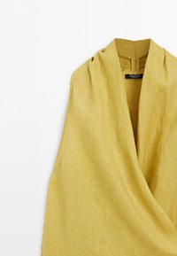 Sleeveless mustard yellow linen top with a deep V-neck and a gathered collar detail, shown from the front on a white background.