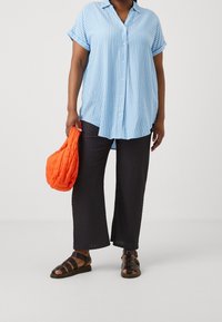 Randig blå skjorta, svarta texturerade vida byxor, svarta sandaletter med remmar och en orange vadderad väska.