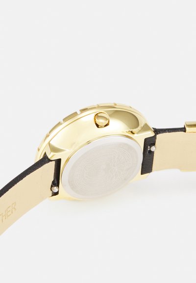 Ceas de aur cu carcasă lustruită și coroana texturată. Dispune de o brățară din piele neagră și un capac din spate gravat de argint.