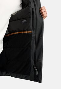 Sort jakke med en glat overflade og fleecefor, prydet med en lille lynlåslomme, orange striber og trykknapper langs forsiden.