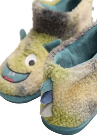 Zapatillas esponjosas verdes y grises con una cara sonriente, tela texturizada y detalles coloridos. Presentan pequeños cuernos y un forro suave.