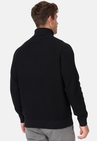 Maglione a collo alto lavorato a maglia nera, con polsini e orlo a coste. Tessuto testurizzato con vestibilità rilassata e maniche raglan.