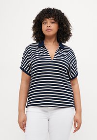 Polo a righe navy e crema con scollatura a V, maniche corte e colletto a tinta unita. Tessuto morbido con una vestibilità rilassata.
