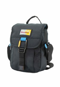 Mochila de tela negra con cierre de solapa, detalles en hardware azul y una etiqueta amarilla. Cuenta con un cierre rápido en la parte frontal y una correa ajustable.