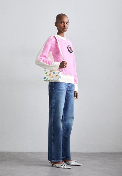 Pink ribbed sweater with white accents and floral patch, paired with light blue wide-leg jeans and silver pointed-toe heels, holding a floral bag.