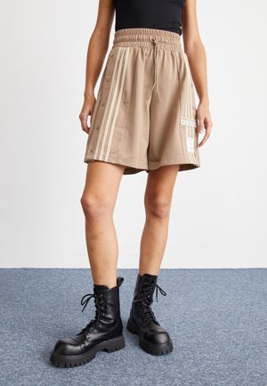 Beige sports shorts with side buttons, three white stripes, and an Adidas logo patch, paired with black lace-up combat boots.